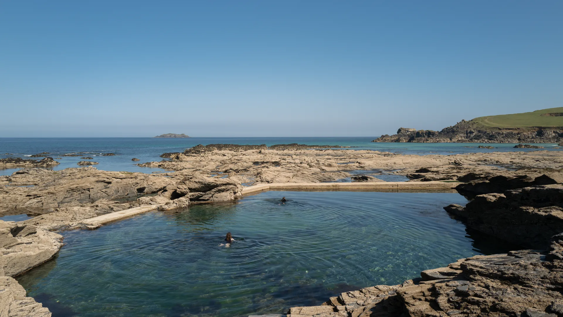 Women in wetsuits walking into the sea on the Cornwall coast